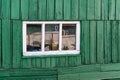 An old wooden small window with a frame of boards painted white and thin glass. On a battered wall of wooden planks with green pai Royalty Free Stock Photo