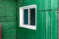 An old wooden small window with a frame of boards painted white and thin glass. On a battered wall of wooden planks with green pai Royalty Free Stock Photo