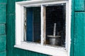 An old wooden small window with a frame of boards painted white and thin glass. On a battered wall of wooden planks with green pai Royalty Free Stock Photo