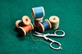 Old wooden spools with multicolored threads and scissors on green cloth. Retro still life. Close-up. Selective focus Royalty Free Stock Photo