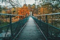 Old wooden suspension bridge over river against background of yellow-orange autumn trees Royalty Free Stock Photo