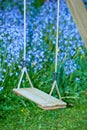 Old wooden swing in a garden with blue flowers and moss in a lush backyard. Peaceful scene of a forgotten playground Royalty Free Stock Photo