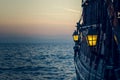 Old wooden vintage pirate ship on sea water surface in sunset evening romantic time with yellow light from soft focus lantern in Royalty Free Stock Photo