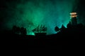 Old wooden warship sailing by night close to lighthouse or lighthouse and sailboat. Dark foggy background. Selective focus. Royalty Free Stock Photo