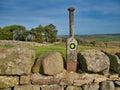 An old wooden way marker on a stile over a stone wall in fields on the Hadrian`s Wall Coast Path in Northumberland, England, UK. Royalty Free Stock Photo