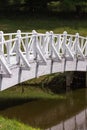 Old wooden white bridge over small pond or lake in city park. Concept of Asian garden design in summer time. Royalty Free Stock Photo