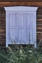 Old wooden window with closed shabby shutters lavender color. Facade of typical rural timber house, Russia