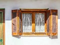 Old wooden window with open shutters on white stucco wall with insect netting tacked on and white lace peacock curtains - part of Royalty Free Stock Photo