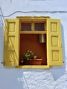 Yellow window in Greece with a flower pot