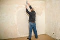 The old worker plastered the wall in the apartment. A man in dirty clothes with a large spatula performs the puttying of the wall Royalty Free Stock Photo