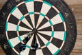 Old worn board for the game of darts with three darts in the center on a wooden wall. Close-up. Selective focus