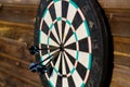 Old worn board for the game of darts with three darts in the center on a wooden wall. Close-up. Selective focus