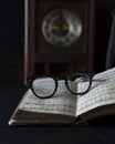 Old worn Glasses resting on an opened book with books and clock in background Royalty Free Stock Photo