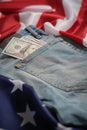 Old worn jeans are lying on flag United States America and there are hundred dollar bills in pocket Royalty Free Stock Photo