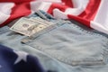 Old worn jeans are lying on flag United States America and there are hundred dollar bills in pocket Royalty Free Stock Photo