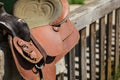 Old worn leather horse saddle on wooden fence, lit by sun. Royalty Free Stock Photo