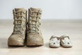 Old worn military boots and baby shoes on wooden floor. Concept of military father and family Royalty Free Stock Photo