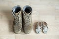 Old worn military boots and baby shoes on wooden floor. Concept of military father and family Royalty Free Stock Photo