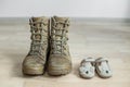 Old worn military boots and baby shoes on wooden floor. Concept of military father and family Royalty Free Stock Photo