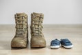 Old worn military boots and baby shoes on wooden floor. Concept of military father and family Royalty Free Stock Photo