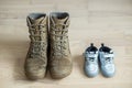 Old worn military boots and baby shoes on wooden floor. Concept of military father and family Royalty Free Stock Photo