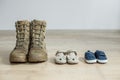 Old worn military boots and baby shoes on wooden floor. Concept of military father and family Royalty Free Stock Photo