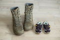 Old worn military boots and children`s shoes on wooden floor. Concept of military father and family