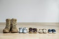 Old worn military boots and lot of baby shoes on wooden floor. Military father and family concept Royalty Free Stock Photo