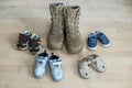 Old worn military boots and lot of baby shoes on wooden floor. Military father and family concept Royalty Free Stock Photo