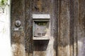 An old, worn, rusted and unlabeled mailbox, mounted on an old weathered wooden door. Next to it is an unlabeled bell