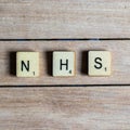 Old worn vintage wooden textured cubes with letters spelling NHS. British National Health Service