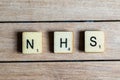 Old worn vintage wooden textured cubes with letters spelling NHS. British National Health Service