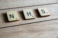 Old worn vintage wooden textured cubes with letters spelling NHS. British National Health Service