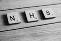 Old worn vintage wooden textured cubes with letters spelling NHS. British National Health Service