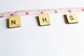 Old worn vintage wooden textured cubes with letters spelling NHS and tape measure depicting 2 meters