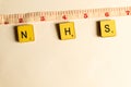 Old worn vintage wooden textured cubes with letters spelling NHS and tape measure depicting 2 meters