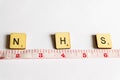 Old worn vintage wooden textured cubes with letters spelling NHS and tape measure depicting 2 meters