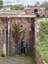 Old, worn wooden basement door on a red brick building with climbing plants and a cannon in the background at Fort Washington, Royalty Free Stock Photo