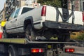 Old wrecked broken pickup vehicle accident transportation on flatbed tow truck machine on city street. Emergency road