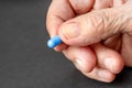 Old wrinkled hand holding a blue pill close up Royalty Free Stock Photo