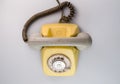 Old yellow antique rotary telephone on blue background. Vintage landline phone with dial, twisted cable and grey Royalty Free Stock Photo