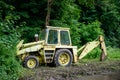 Old yellow backhoe loader parked at forest edge with overgrown vegetation Royalty Free Stock Photo