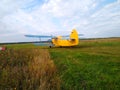 An old yellow biplane with blue wings and a running engine drives through a field of green grass Royalty Free Stock Photo