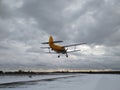 Old yellow biplane plane flies over a dirt runway in winter with snow against a blue sky Royalty Free Stock Photo