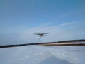 Old yellow biplane plane flies over a dirt runway in winter with snow against a blue sky Royalty Free Stock Photo