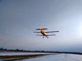 Old yellow biplane plane flies over a dirt runway in winter with snow against a blue sky Royalty Free Stock Photo