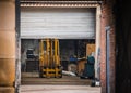 Old yellow fork lift truck parked in garage with roller shutter door down. Undergoing repair and maintenance in old workshop Royalty Free Stock Photo