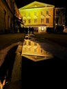 Old yellow house in reflection of puddle on pavement. European vintage city view