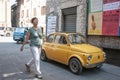 Old yellow small vintage car parked in old town street under wall of posters in Italian language Royalty Free Stock Photo