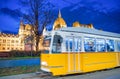 Old yellow tram speeds up along city streets at night. The historical center of the capital of Hungary